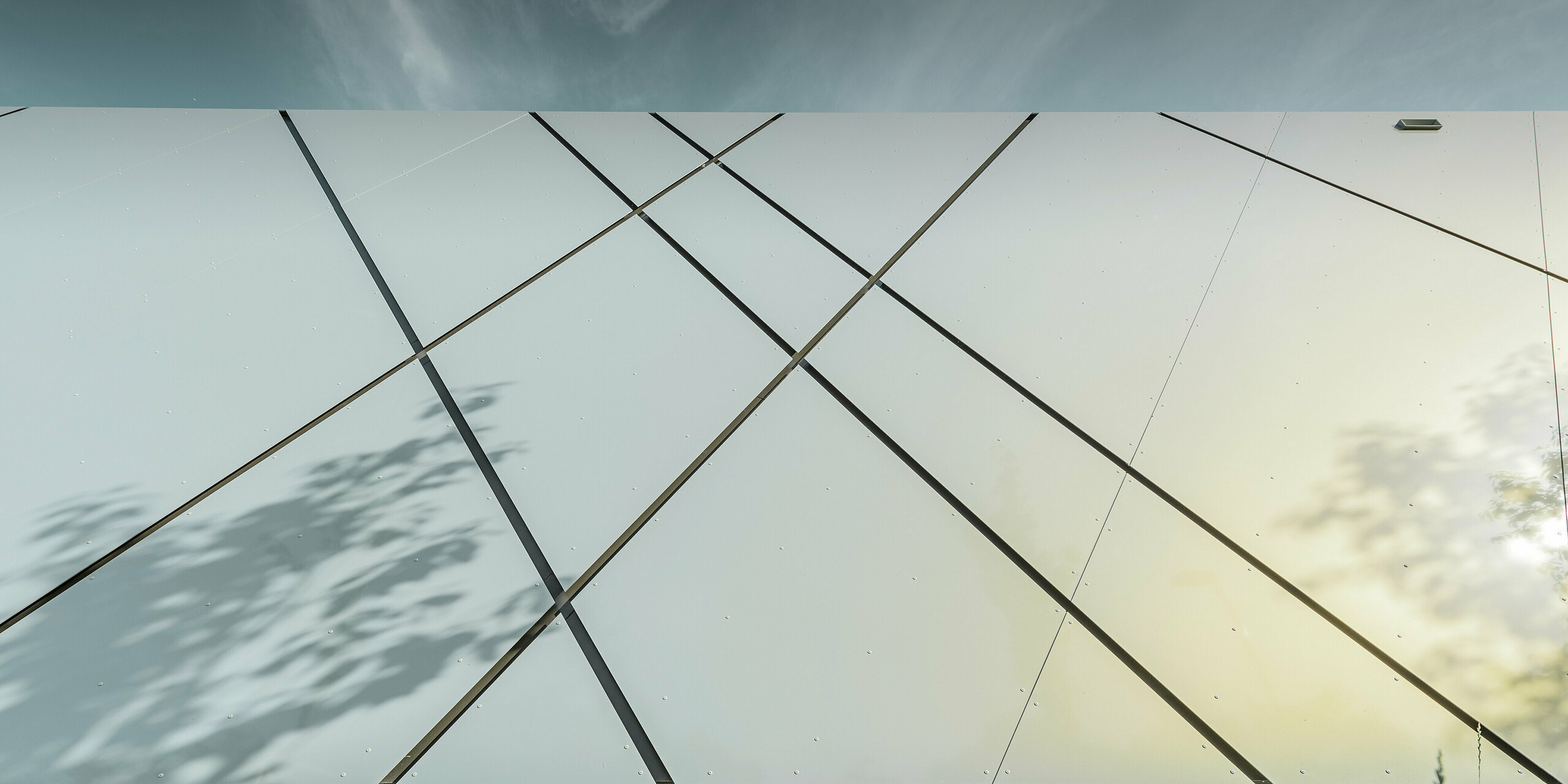 Die Nahaufnahme der PREFA Fassade verdeutlicht die präzise Anordnung der genieteten Aluminium Verbundplatten in Silver gold. Die kontrastreichen, diagonal verlaufenden Fugen erzeugen ein raffiniertes Spiel aus Geometrie, Glanz und Struktur an der Außenhaut der Eurospar Filiale in Wels.