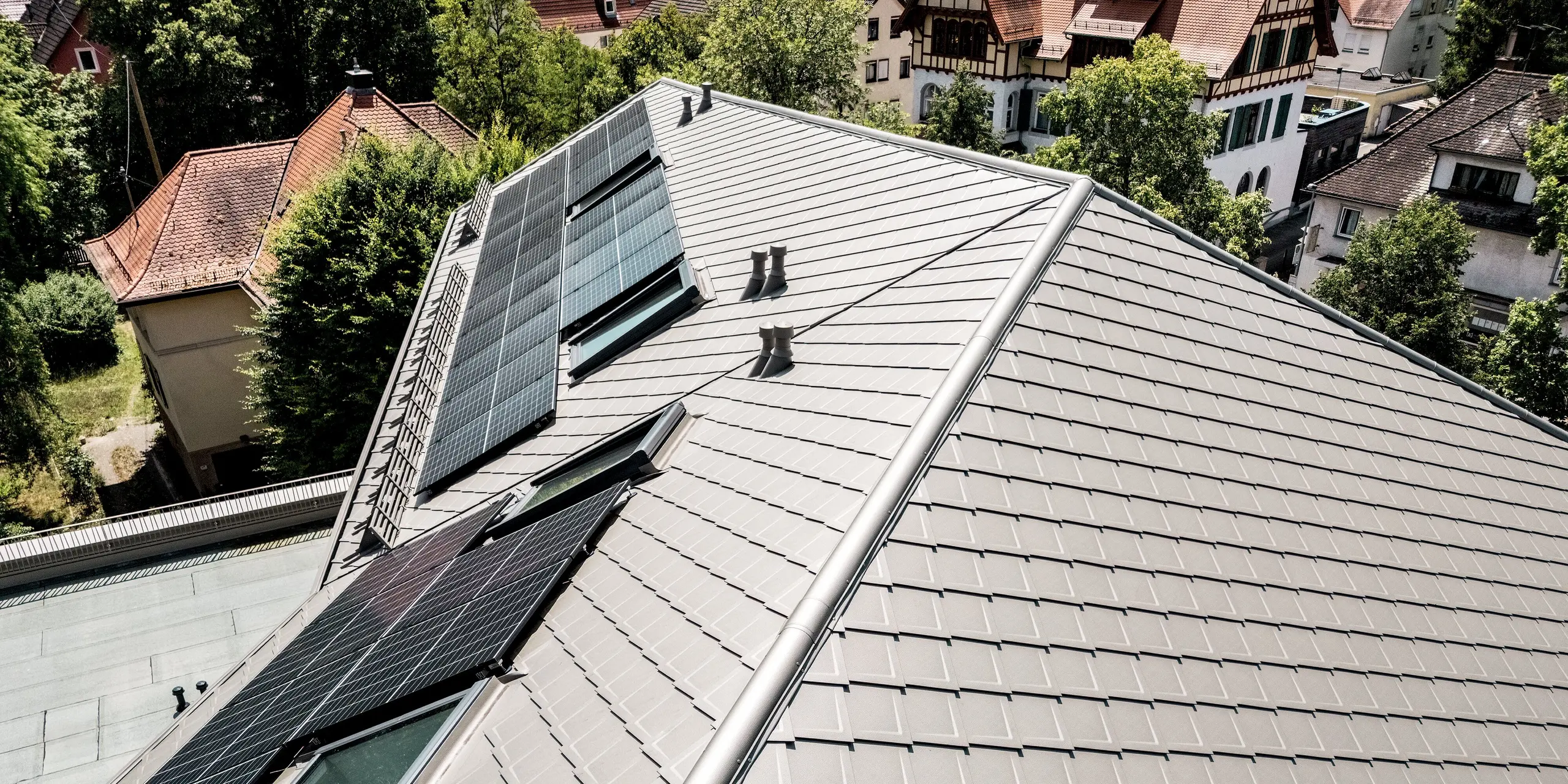 Spektakuläre Luftaufnahme der Sparkasse Blaubeuren: Die PREFA Dachrauten 44 × 44 in Bronze verleihen der weitläufigen Dachlandschaft eine elegante, geometrische Struktur. Großflächige Photovoltaikanlagen und integrierte Dachfenster setzen moderne Akzente. Die leichten, langlebigen und witterungsbeständigen Aluminium-Dachrauten vereinen zeitlose Ästhetik mit hoher Funktionalität und harmonieren mit der historischen Umgebung.