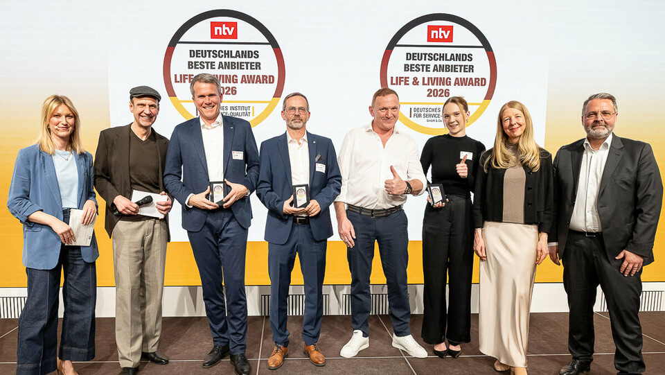 Tobias Götz, Geschäftsführer von PREFA, steht gemeinsam mit weiteren Preisträgerinnen und Preisträgern auf der Bühne beim Life & Living Award 2026 und präsentiert die erhaltene Auszeichnung.