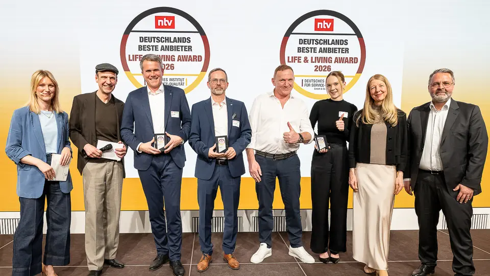 Tobias Götz, Geschäftsführer von PREFA, steht gemeinsam mit weiteren Preisträgerinnen und Preisträgern auf der Bühne beim Life & Living Award 2026 und präsentiert die erhaltene Auszeichnung.