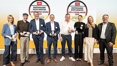 Tobias Götz, Geschäftsführer von PREFA, steht gemeinsam mit weiteren Preisträgerinnen und Preisträgern auf der Bühne beim Life & Living Award 2026 und präsentiert die erhaltene Auszeichnung.