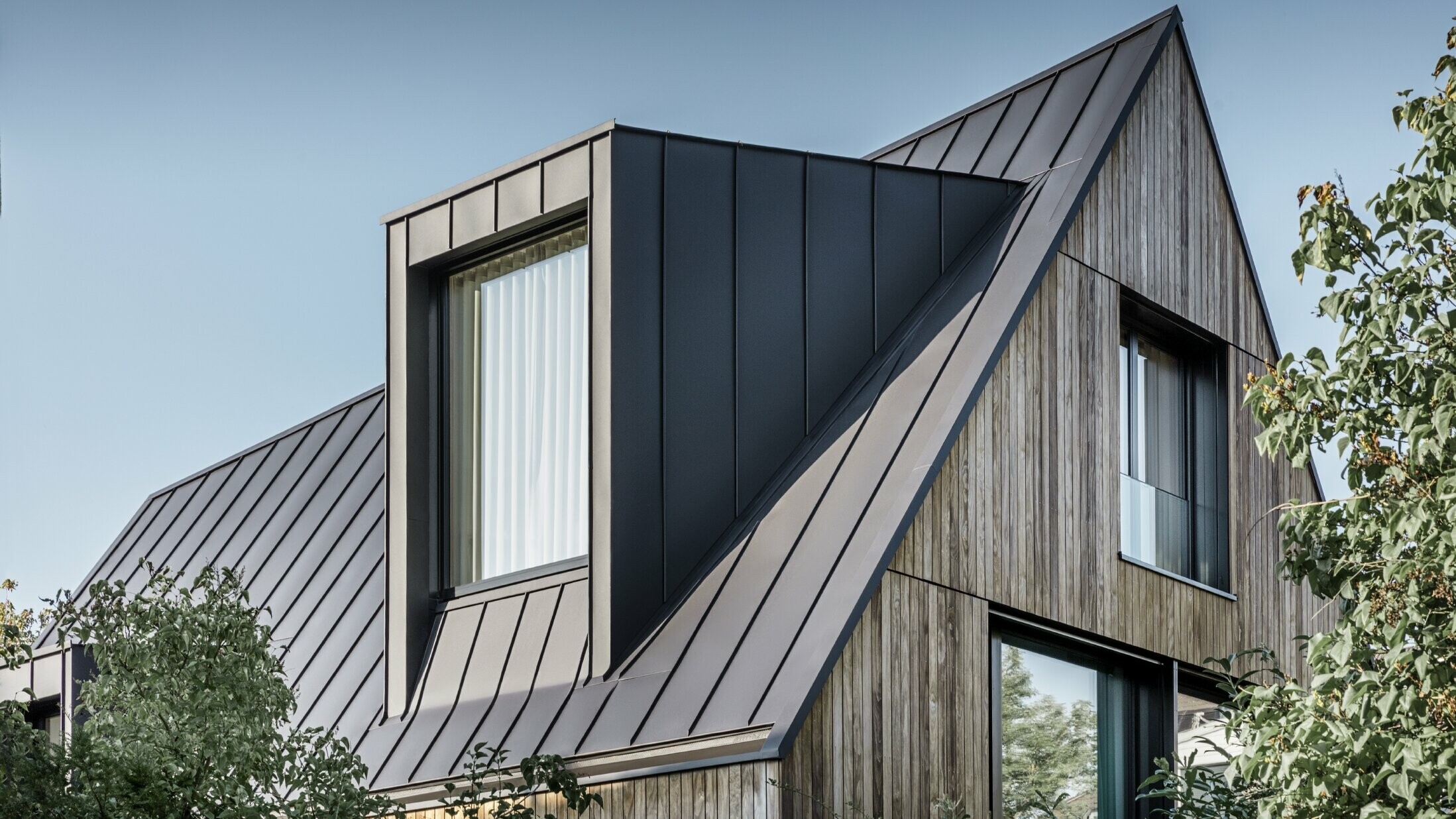 Steiles Satteldach mit großer Gaube, eingedeckt mit PREFALZ von PREFA in Anthrazit Stehfalzdach kombiniert mit Holzfassade
