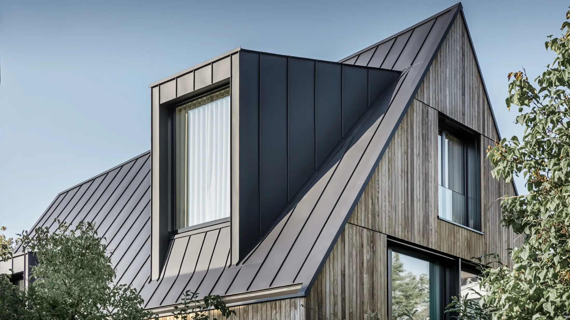 Steiles Satteldach mit großer Gaube, eingedeckt mit PREFALZ von PREFA in Anthrazit Stehfalzdach kombiniert mit Holzfassade