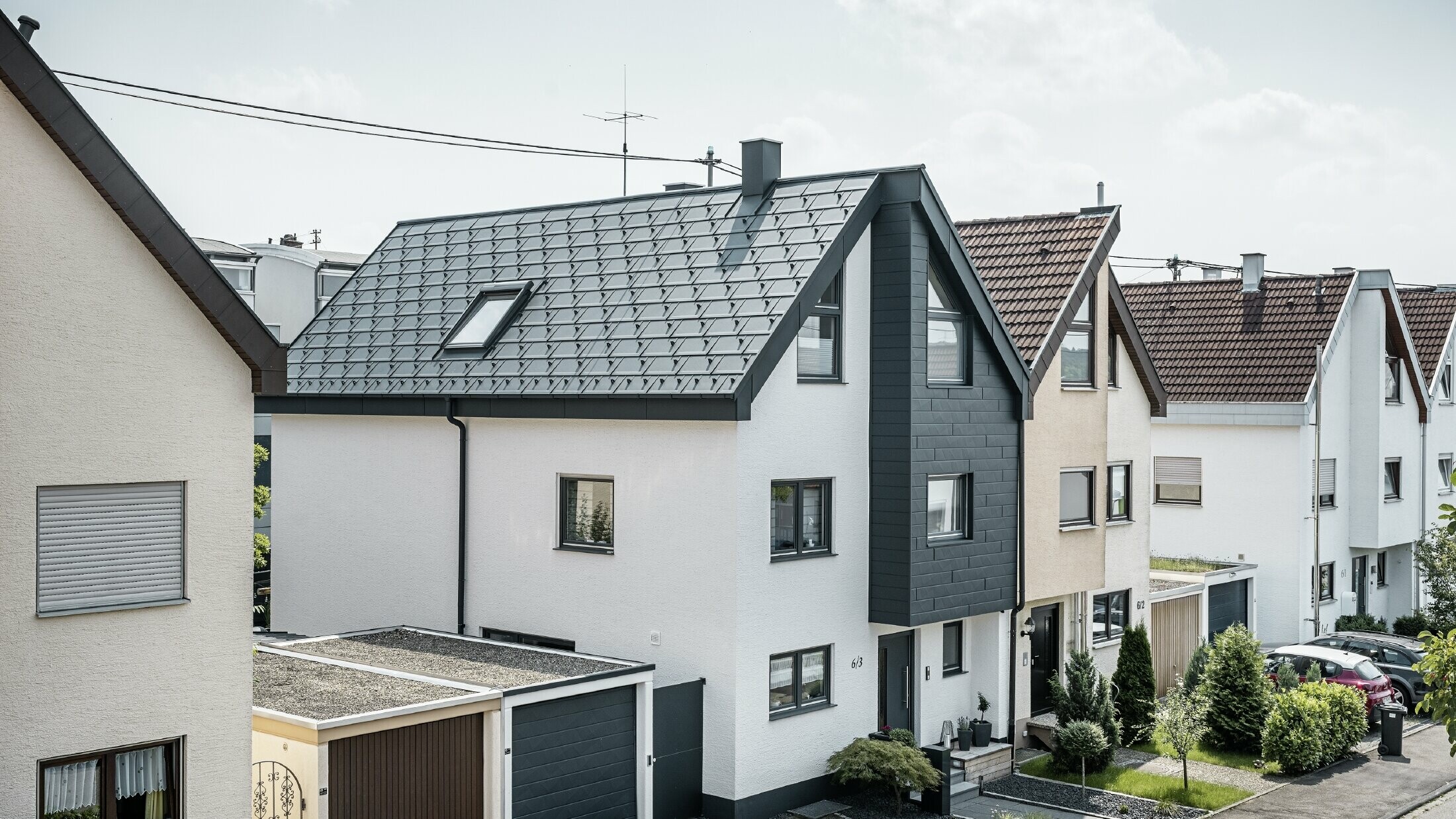 Eine Doppelhaushälfte wurde bereits saniert, mit frischer weißer Putzfassade, kombiniert mit einer PREFA Siding.X Fassade in Anthrazit. Das Dach wurde mit der PREFA Dachplatte R.16 eingedeckt. Die Dachentwässerung erfolgt über die eckige Kastenrinne inklusive PREFA Ablaufrohr.