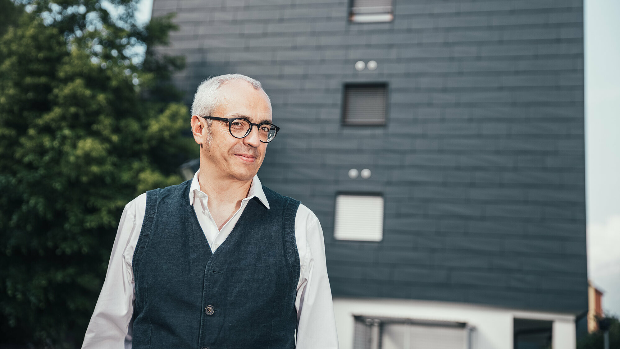 Portrait von Architekt Manuel Benedikter vor dem thermisch sanierten Wohnbau mit der anthrazitfarbenen PREFA Fassade.