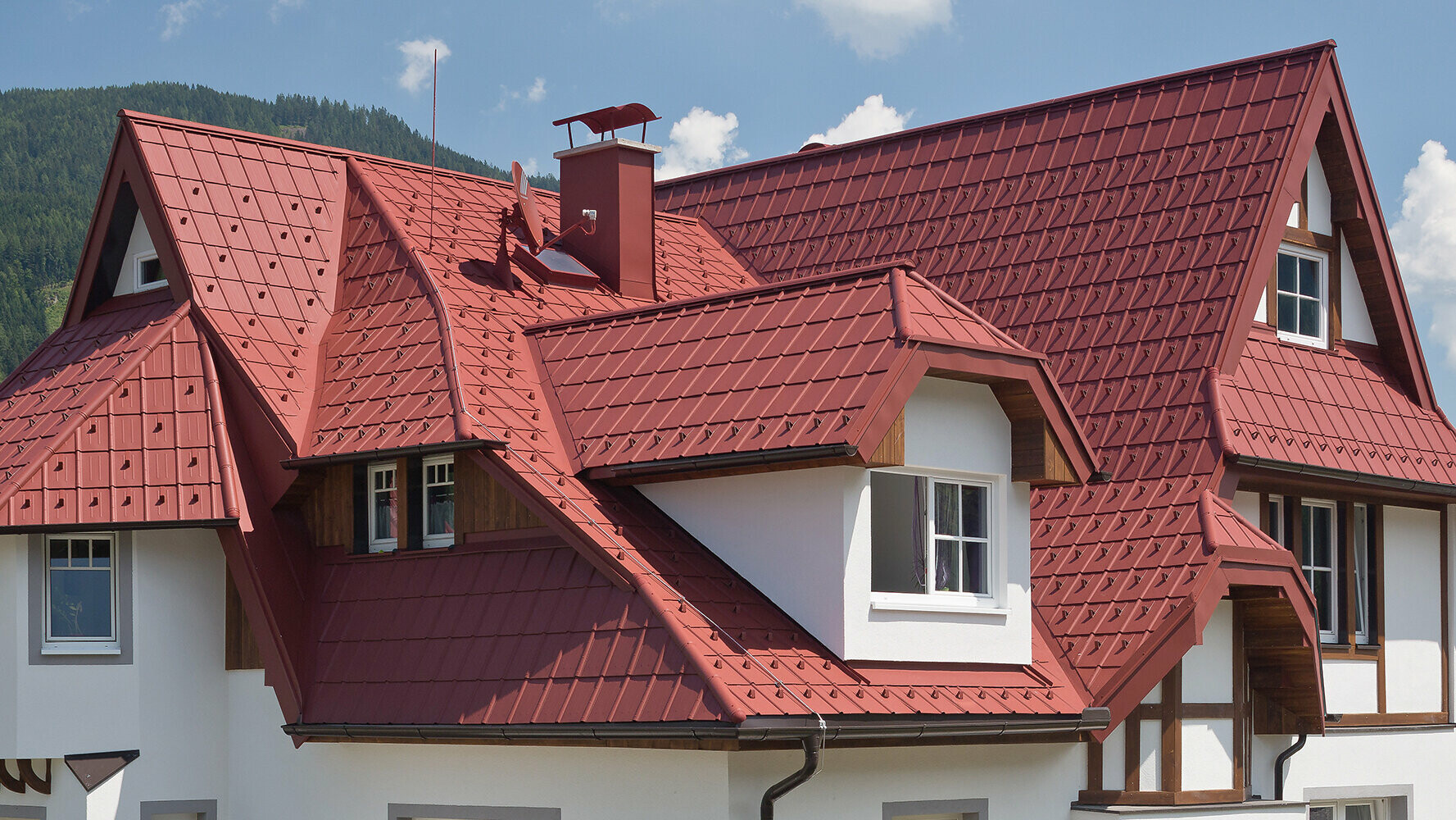 Einfamilienhaus mit verwinkelter Dachlandschaft, vielen Details und Gauben; Eingedeckt mit der PREFA Dachplatte in Oxydrot.