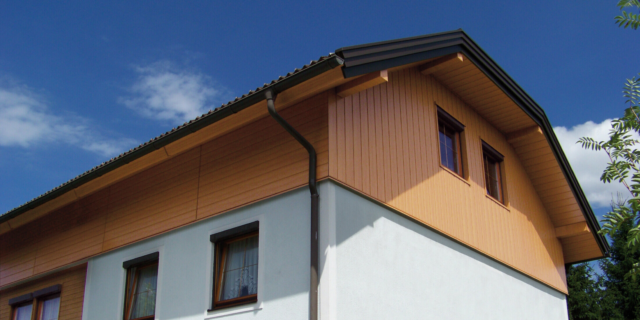 Großes Einfamilienhaus mit Krüppelwalmdach und einer Giebelverkleigung mit den PREFA Sidings in Holzoptik (Farbe Eiche natur)