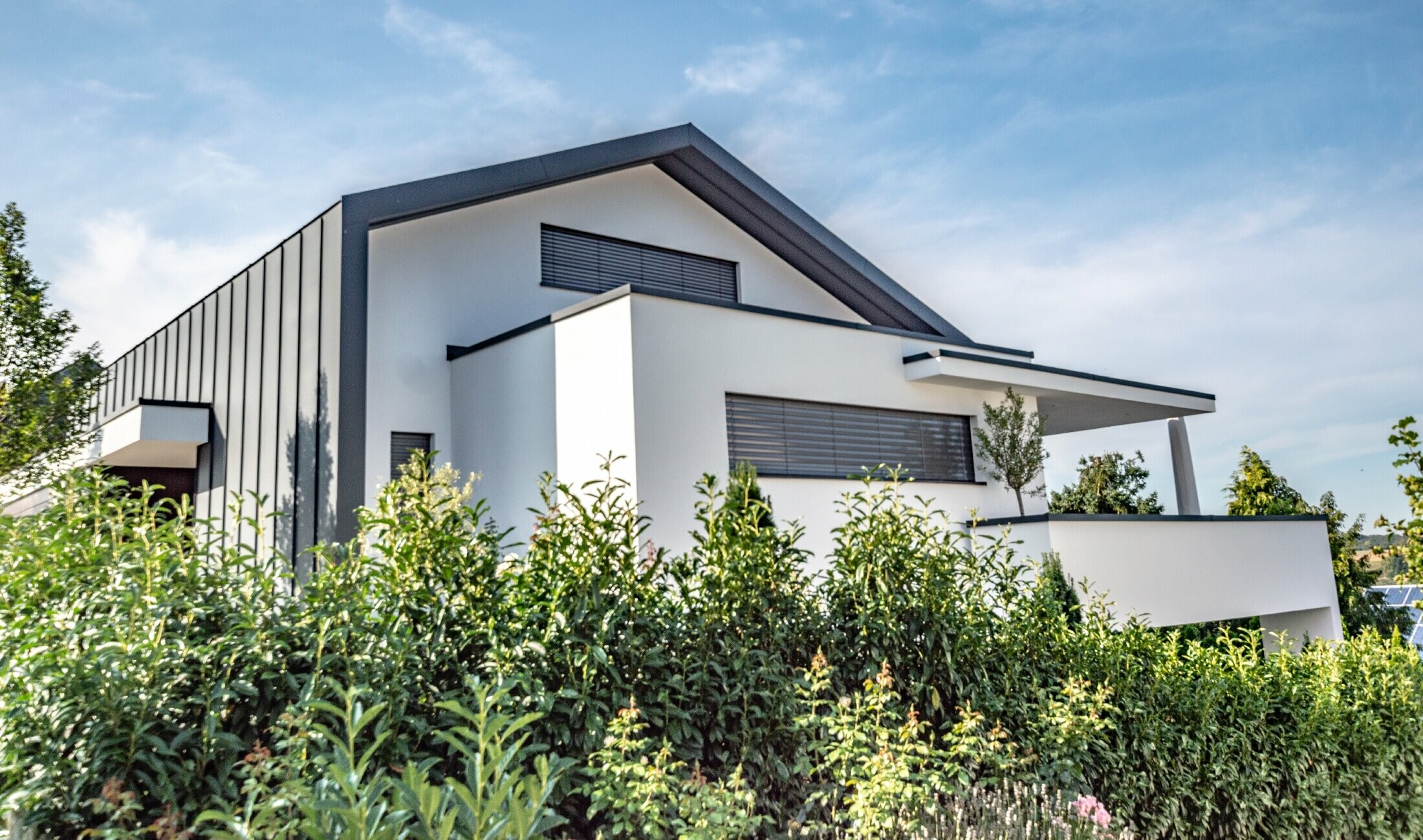 Modernes Einfamilienhaus, bei dem sich die Dacheindeckung als Stehfalzverkleidung auch über die Fassade zieht. Die Farbe des PREFA Materials ist anthrazit.