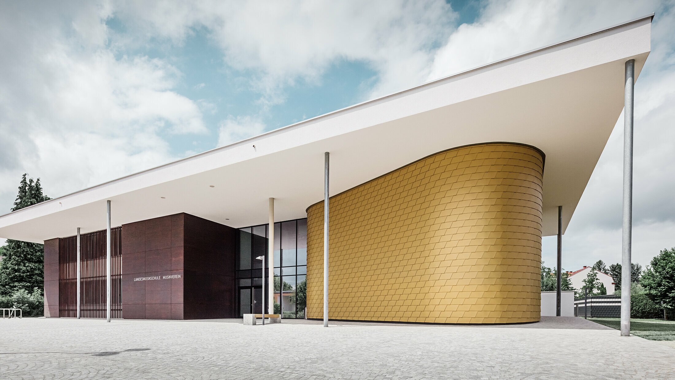 Goldene Aluminiumschindeln von PREFA schmücken die gerundete Fassade der Musikschule