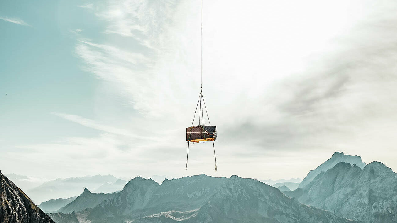 Der fliegende Transport des Informationskiosks zum fixen Standort in den Bergen Vorarlbergs.