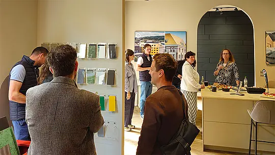 Mehrere Besucher im PREFA Showroom Berlin bei der offiziellen Neueröffnung des Schauraums. Die Interessenten stehen vor einer Wand mit verschiedenen Farb- und Materialmustern. Im Hintergrund sieht man ein paar Poster von fertigen PREFA Referenzobjekten.