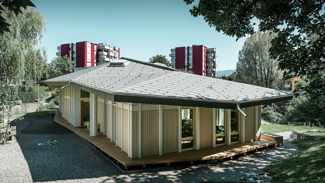 Eingeschossiger Kindergarten mit senkrechten Fassadenpaneelen und Alu-Dach von PREFA (Dachraute) in Hellgrau
