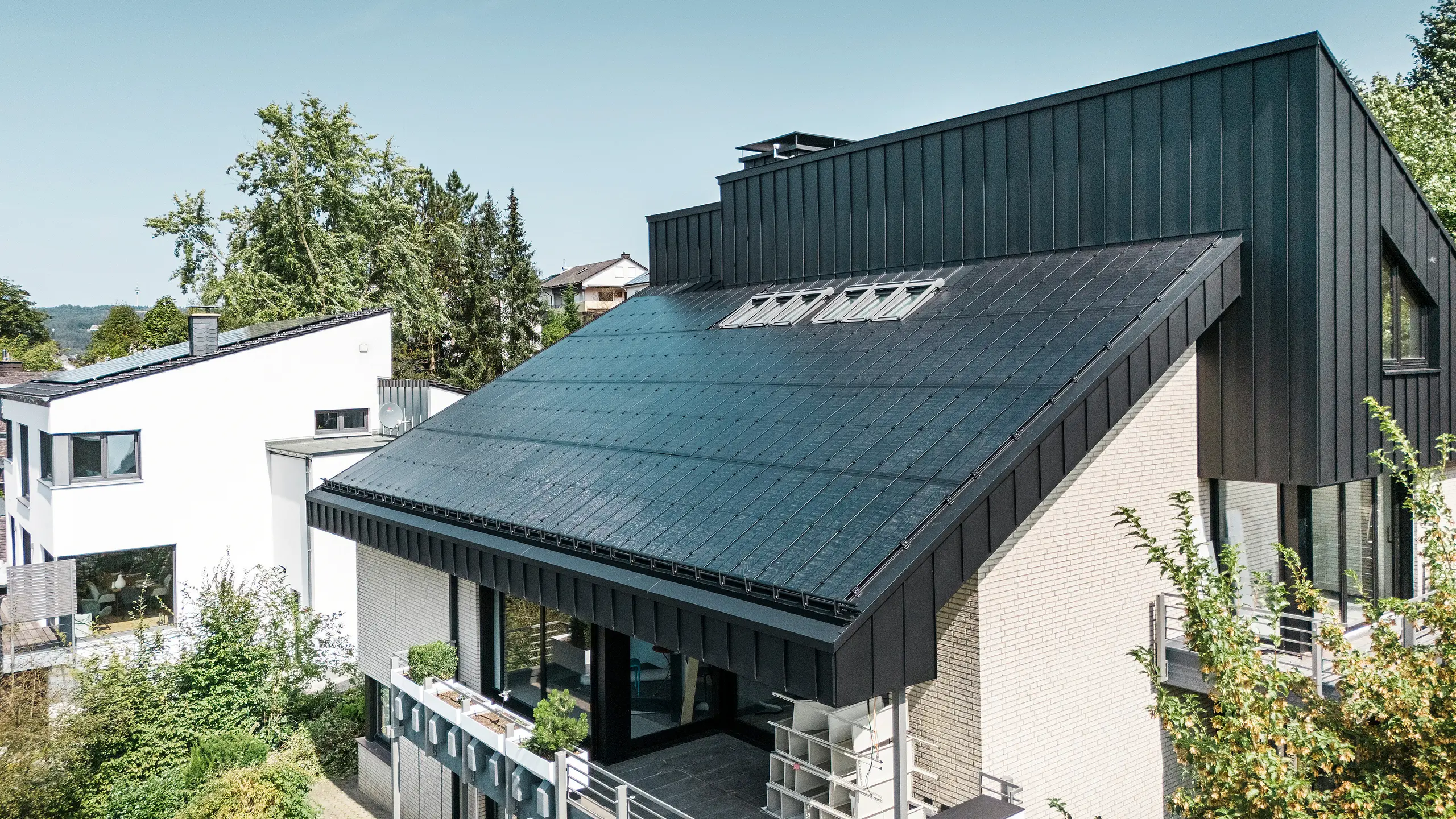 Moderne Architektur eines Einfamilienhauses in Meschede, Deutschland, mit einem PREFALZ-Aluminiumdach in P.10 Schwarz und integrierten Glas/Glas-Photovoltaikmodulen. Das versetzte Dach vereint zeitloses Design mit nachhaltiger Photovoltaik-Technologie. Die innovativen PREFALZ-Solarmodule liefern eine Leistung von 18 kWp. Die rahmenlosen Module und die elegante Aluminium-Dach- und Fassadenverkleidung bilden ein ästhetisches und funktionales Ganzes, das sich harmonisch in die grüne Wohnumgebung einfügt.