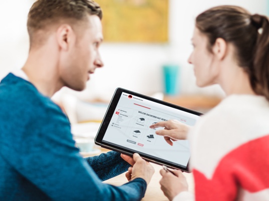 Junges Pärchen nutzt die PREFA Plattform um schnell an ein Angebot für ihr neues Dach und ihre neue Fassade zu kommen. Sie navigieren durch den Fragebogen auf einem Tablet.