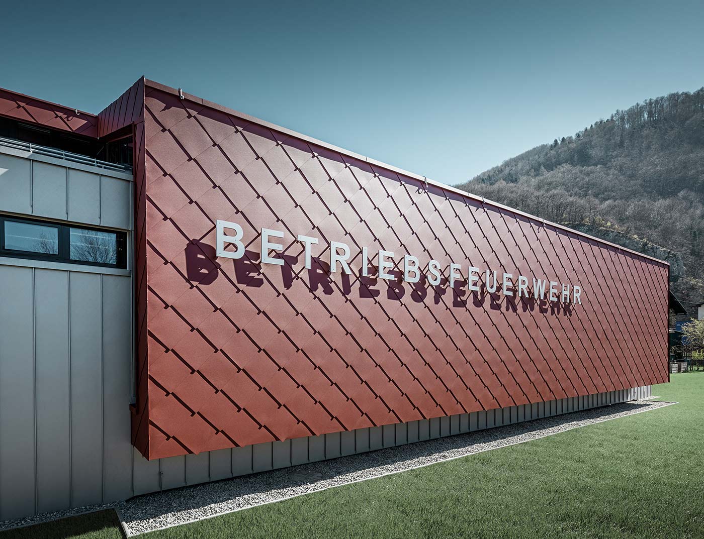 Ein Teil der Fassade der Betriebsfeuerwehr der Firma Neuman und PREFA in Marktl wurde mit der Aluwandraute 44 × 44 in Oxydrot verkleidet, darauf wurde der Schriftzug "Betriebsfeuerwehr" installiert.